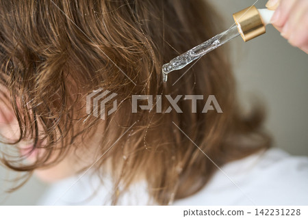 Hand Holding Dropper Dripping Clear Hair Serum Onto Midlength Damp Brown Hair Strands With Droplets Hand Holding Dropper Dripping Clear Hair Serum Onto Midlength Damp Brown Hair Strands With Droplets 142231228