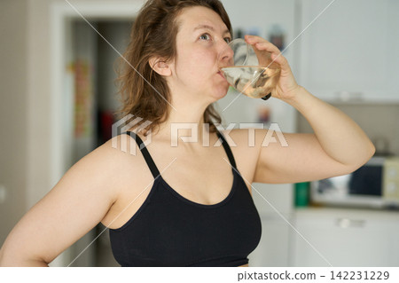 Woman Tilting Head Back While Drinking From Glass In Kitchen Near Cabinets Microwave Woman Tilting Head Back While Drinking From Glass In Kitchen Near Cabinets Microwave 142231229