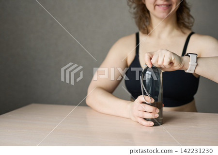 Woman Opening Translucent Gray Water Bottle While Seated At Wooden Table In Minimalist Indoor Woman Opening Translucent Gray Water Bottle While Seated At Wooden Table In Minimalist Indoor 142231230