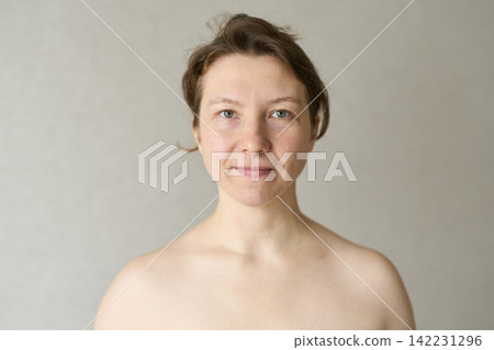 Woman Facing Camera Neutral Expression Standing Against Plain Indoor Background With Bare Shoulders Woman Facing Camera Neutral Expression Standing Against Plain Indoor Background With Bare Shoulders 142231296