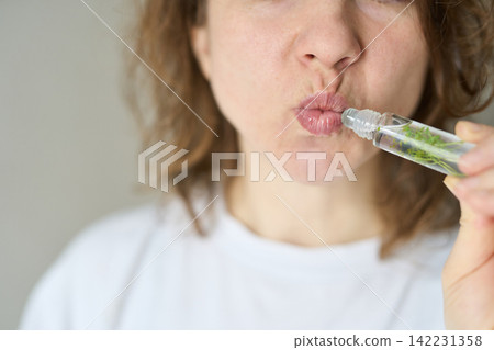Woman Puckering Lips Applying Roller Lip Gloss With Botanical Fragments In Transparent Bottle Woman Puckering Lips Applying Roller Lip Gloss With Botanical Fragments In Transparent Bottle 142231358