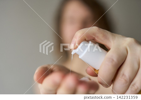 Woman Dispensing Liquid From Pump Bottle Into Open Palm With Blurred Face In Background Indoor 142231359