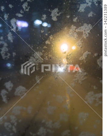 Fogged And Saltstreaked Window With Blurred Streetlight Glow And Scattered Flakes Viewed From Fogged And Saltstreaked Window With Blurred Streetlight Glow And Scattered Flakes Viewed From 142231389