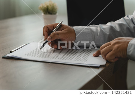 Close-up of hands using a pen to review printed paperwork on a clipboard at a desk, showing document verification, contract terms review and an office approval workflow with copy space. Close-up of hands using a pen to review printed paperwork on a clipboard at a desk, showing document verification, contract terms review and an office approval workflow with copy space. 142231421