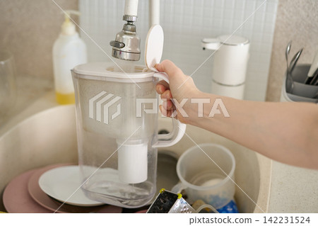 Water Filter Pitcher Being Held Open Under Faucet Over Kitchen Sink With Dishes Soap Dispenser Water Filter Pitcher Being Held Open Under Faucet Over Kitchen Sink With Dishes Soap Dispenser 142231524