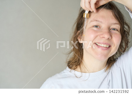 Woman Holding Dropper Above Face While Dispensing Facial Oil In Indoor Home Setting With Neutral Woman Holding Dropper Above Face While Dispensing Facial Oil In Indoor Home Setting With Neutral 142231592