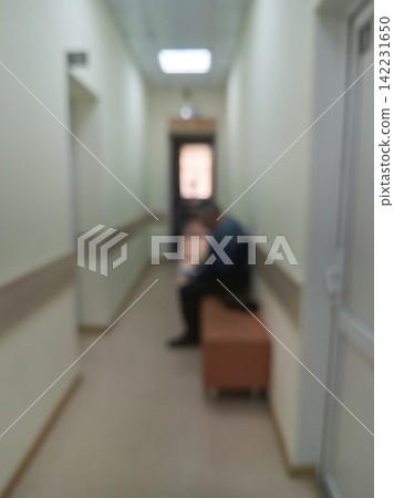 Blurred Person Sitting On Bench In Long Hospital Corridor Waiting Area With Fluorescent Ceiling Blurred Person Sitting On Bench In Long Hospital Corridor Waiting Area With Fluorescent Ceiling 142231650
