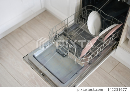 Dishwasher Rack With Pink And White Plates Open And Partially Loaded On Tiled Kitchen Floor Near Dishwasher Rack With Pink And White Plates Open And Partially Loaded On Tiled Kitchen Floor Near 142231677
