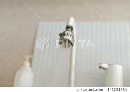 Overhead View Of White Kitchen Spout Releasing Narrow Stream Of Water Against Tiled Wall With Soap Overhead View Of White Kitchen Spout Releasing Narrow Stream Of Water Against Tiled Wall With Soap 142231684