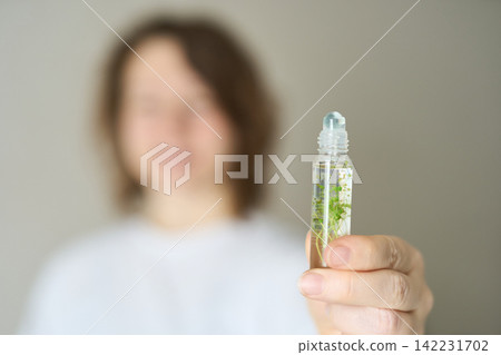 Person Presenting Rollon Bottle To Camera With Focus On Small Glass Vial Containing Green Plant Person Presenting Rollon Bottle To Camera With Focus On Small Glass Vial Containing Green Plant 142231702