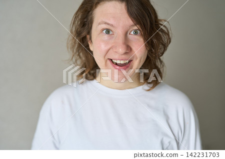 Woman Smiling With Surprised Expression Standing Indoors Against Plain Neutral Background Wearing Woman Smiling With Surprised Expression Standing Indoors Against Plain Neutral Background Wearing 142231703