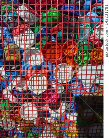 Assorted Plastic Bottle Caps Pressed Against Red Metal Grid Forming Dense Colorful Mosaic Assorted Plastic Bottle Caps Pressed Against Red Metal Grid Forming Dense Colorful Mosaic 142231781