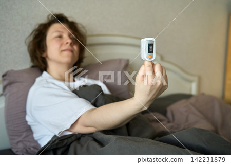 Woman In Bed Using Pulse Oximeter Device To Measure Oxygen Saturation Illustrating Home Healthcare Woman In Bed Using Pulse Oximeter Device To Measure Oxygen Saturation Illustrating Home Healthcare 142231879