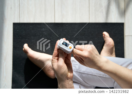 Person Checking Oxygen Level Using Pulse Oximeter While Sitting Barefoot On Yoga Mat On Light Wood Person Checking Oxygen Level Using Pulse Oximeter While Sitting Barefoot On Yoga Mat On Light Wood 142231982