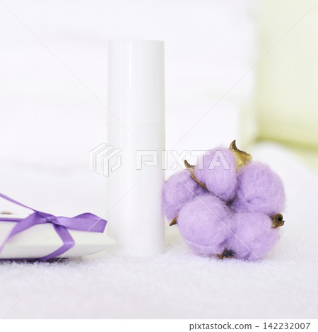 White Cosmetic Bottle Standing Upright Beside Purple Cotton Boll Cluster And Tied Ribbon On White White Cosmetic Bottle Standing Upright Beside Purple Cotton Boll Cluster And Tied Ribbon On White 142232007