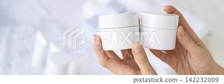 Hands Holding Two White Cosmetic Jars Together In Bright Minimal Skincare Setting Closeup Product Hands Holding Two White Cosmetic Jars Together In Bright Minimal Skincare Setting Closeup Product 142232009