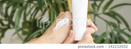 Close Up Of Hands Holding Cosmetic Tube With Cream On Skin Against Green Plant Background Close Up Of Hands Holding Cosmetic Tube With Cream On Skin Against Green Plant Background 142232032