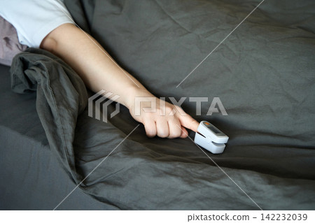 Person Reaching With Finger Toward Pulse Oximeter Placed On Bed Sheet While Partially Covered Person Reaching With Finger Toward Pulse Oximeter Placed On Bed Sheet While Partially Covered 142232039
