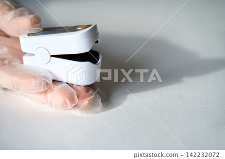 Pulse Oximeter Device Held By Gloved Hand Measuring Finger On White Tabletop In Clinical Close Up Pulse Oximeter Device Held By Gloved Hand Measuring Finger On White Tabletop In Clinical Close Up 142232072