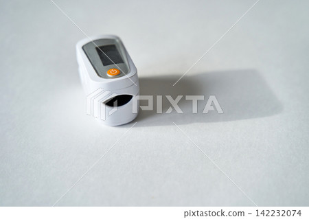 Pulse Oximeter Resting On White Table Top Displaying Power Button And Shadow Close Up Portable Pulse Oximeter Resting On White Table Top Displaying Power Button And Shadow Close Up Portable 142232074