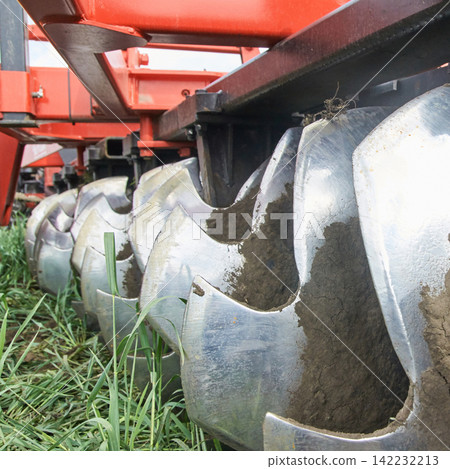 Angle View Of Shiny Scalloped Disc Harrow Blades Filled With Mud While Connected To Red Farm Angle View Of Shiny Scalloped Disc Harrow Blades Filled With Mud While Connected To Red Farm 142232213
