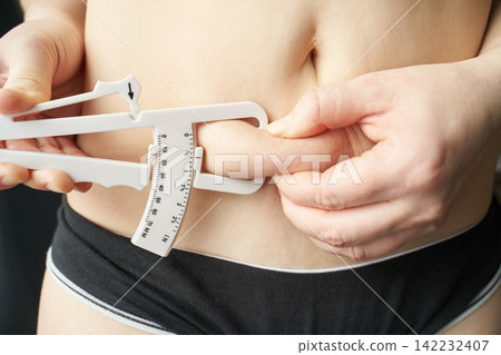 Adult caucasian female measuring body fat with caliper health, fitness, and self-assessment Adult caucasian female measuring body fat with caliper health, fitness, and self-assessment 142232407