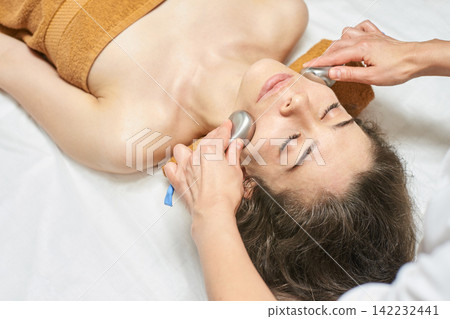 Female Caucasian Adult Receiving Relaxing Facial Massage With Natural Stone Therapy In Spa Setting Female Caucasian Adult Receiving Relaxing Facial Massage With Natural Stone Therapy In Spa Setting 142232441