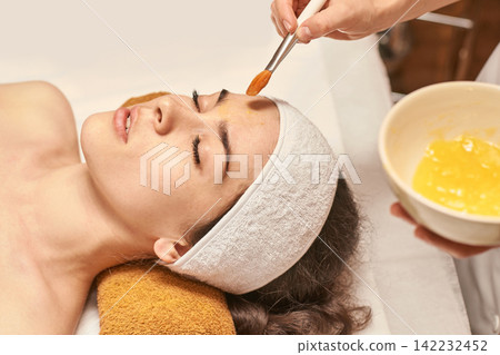 Young Caucasian Female Relaxing During Spa Facial Treatment With Rejuvenating Face Mask Application Young Caucasian Female Relaxing During Spa Facial Treatment With Rejuvenating Face Mask Application 142232452