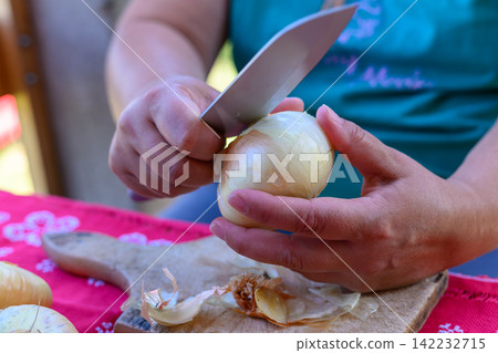 Closeup of a chefs hand slicing a fresh white onion on a wooden cutting board Closeup of a chefs hand slicing a fresh white onion on a wooden cutting board 142232715