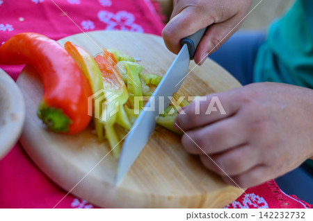 Person slicing a fresh red and green bell pepper on a wooden cutting board Person slicing a fresh red and green bell pepper on a wooden cutting board 142232732
