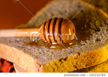 Golden honey and fresh bread slices beside glass jar in warm rustic kitchen setting Golden honey and fresh bread slices beside glass jar in warm rustic kitchen setting 142232784