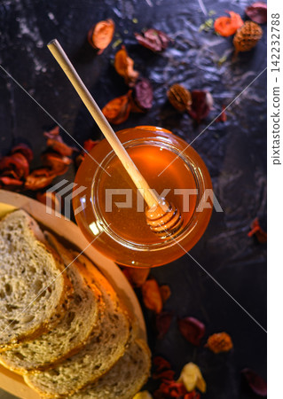 Golden honey and fresh bread slices beside glass jar in warm rustic kitchen setting Golden honey and fresh bread slices beside glass jar in warm rustic kitchen setting 142232788