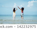 Two girls stand in shallow ocean water, arms raised 142232975