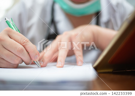 Close up of healthcare professional writing medical notes paper beside laptop showing clinical documentation patient records hospital administration Close up of healthcare professional writing medical notes paper beside laptop showing clinical documentation patient records hospital administration 142233399