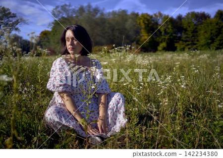 a pregnant mature woman in light dress posing in blooming wild flower field a pregnant mature woman in light dress posing in blooming wild flower field 142234380