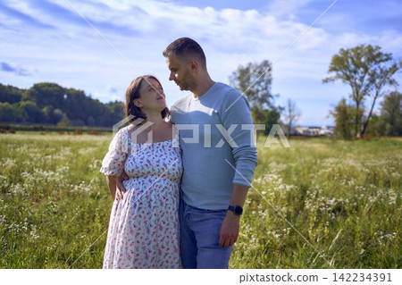 mature couple expecting baby posing together in wild flower meadow in summer mature couple expecting baby posing together in wild flower meadow in summer 142234391