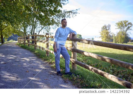 handsome mature man smiling while standing on sunny countryside path 142234392