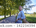 handsome mature man smiling while standing on sunny countryside path 142234394