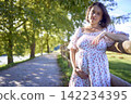 pregnant mature woman in floral dress walking on sunny rural pathway 142234395