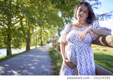 pregnant mature woman in floral dress walking on sunny rural pathway pregnant mature woman in floral dress walking on sunny rural pathway 142234395