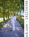 pregnant mature woman in floral dress walking on sunny rural pathway 142234398