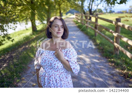 pregnant mature woman in floral dress walking on sunny rural pathway pregnant mature woman in floral dress walking on sunny rural pathway 142234400