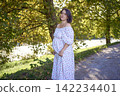 pregnant mature woman in floral dress walking on sunny rural pathway 142234401