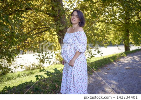 pregnant mature woman in floral dress walking on sunny rural pathway pregnant mature woman in floral dress walking on sunny rural pathway 142234401
