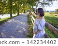 pregnant mature woman in floral dress walking on sunny rural pathway 142234402