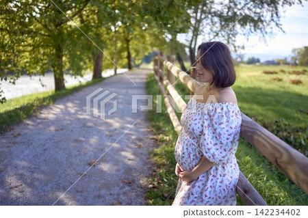 pregnant mature woman in floral dress walking on sunny rural pathway pregnant mature woman in floral dress walking on sunny rural pathway 142234402