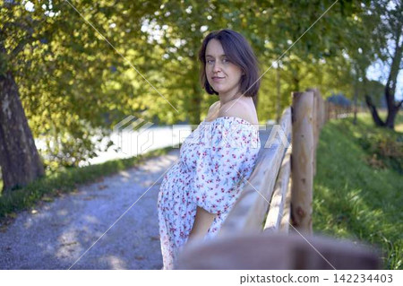pregnant mature woman in floral dress walking on sunny rural pathway pregnant mature woman in floral dress walking on sunny rural pathway 142234403
