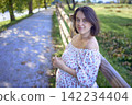 pregnant mature woman in floral dress walking on sunny rural pathway 142234404