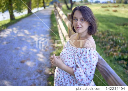 pregnant mature woman in floral dress walking on sunny rural pathway pregnant mature woman in floral dress walking on sunny rural pathway 142234404