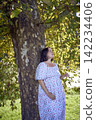 pregnant mature woman in floral dress walking on sunny rural pathway 142234406